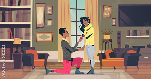 man kneeling holding engagement ring proposing woman marry him happy valentines day concept african american couple in love marriage offer living room interior horizontal