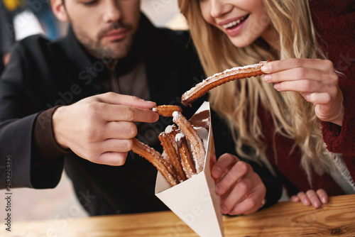 Close-up of young couple are eating churros at the street food market. photo