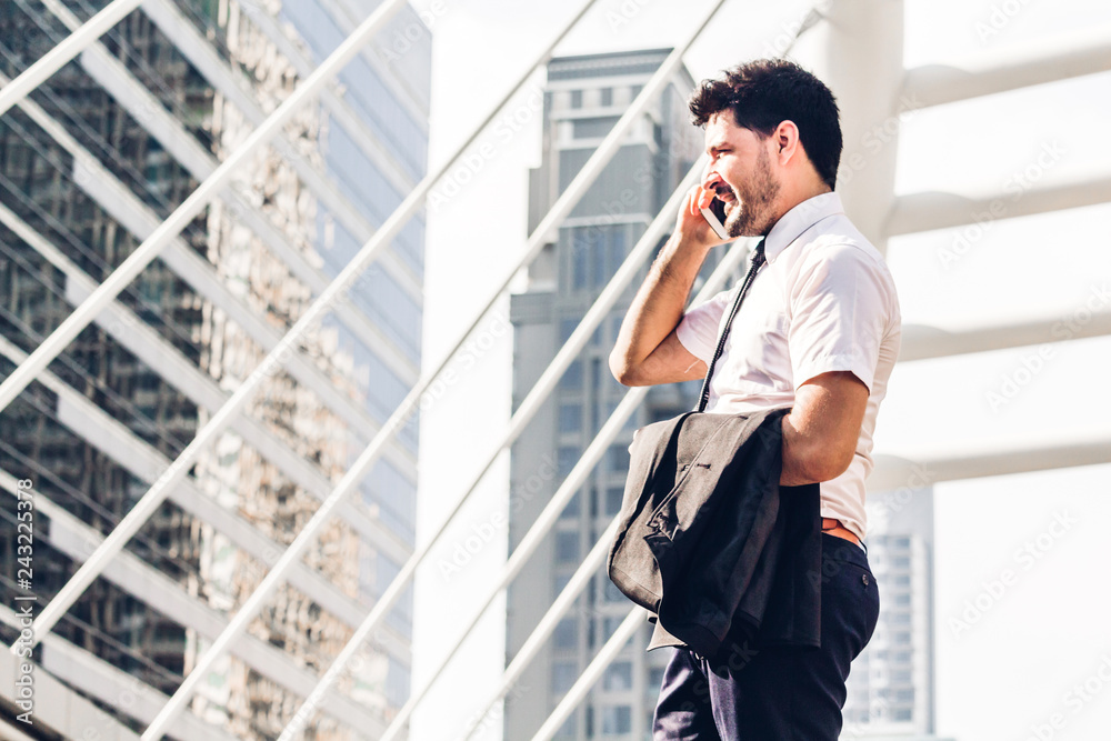 Fototapeta premium Portrait of handsome businessman in black suit standing and using smartphone outdoors on modern city background.man working with technology devices concept