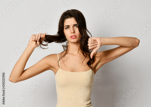 Frustrated brunette woman examining dry damaged hair over gray 