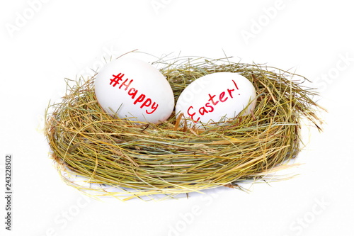 Two chicken eggs in straw nest with text happy Easter and sign hashtag for social network on white background. Isolated