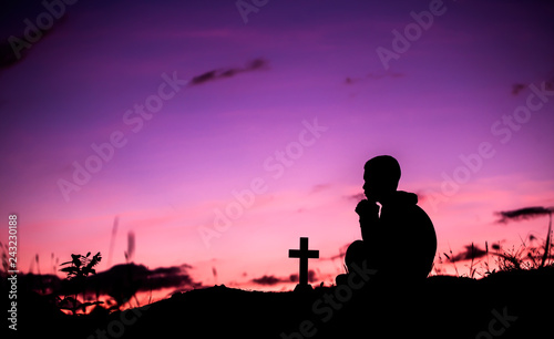 Boy praying to god with cross, christian silhouette concept.
