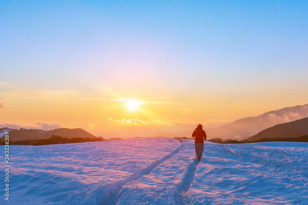 Nature photographer on a snowy field at sunset time