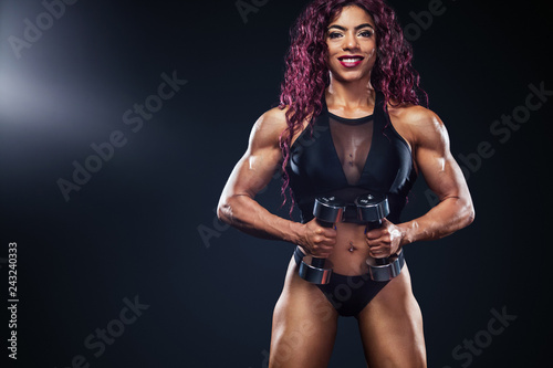 Sporty fit woman  athlete  egyptian and muslim with dumbbells makes fitness exercising on black background with lights.