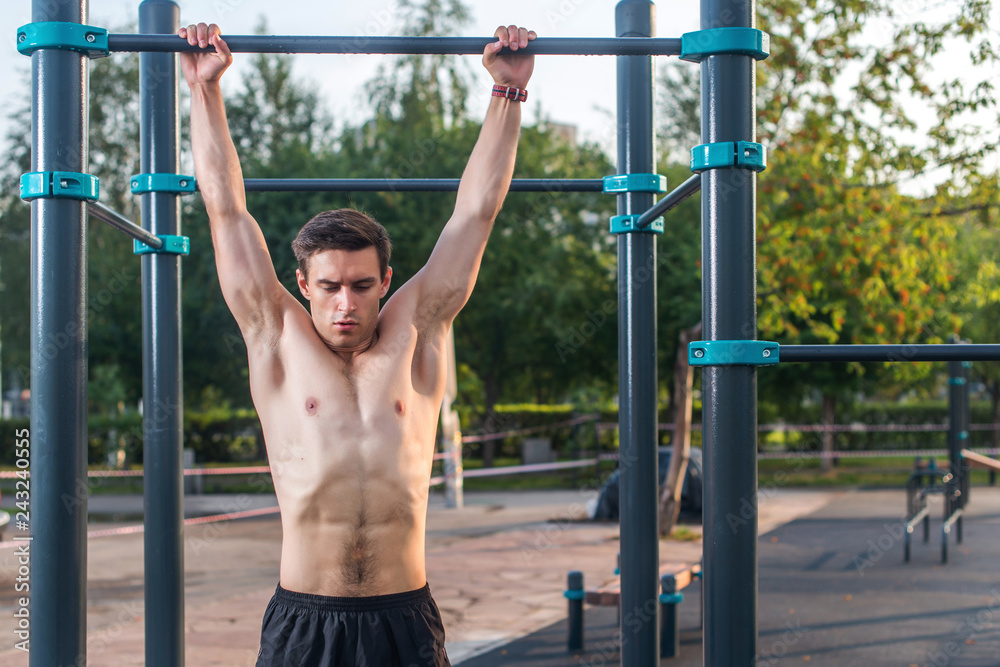 Young male athlete doing chin-up exercises in the park. Fitness man working out outside Young male athlete doing chin-up exercises in the park. Fitness man working out outside