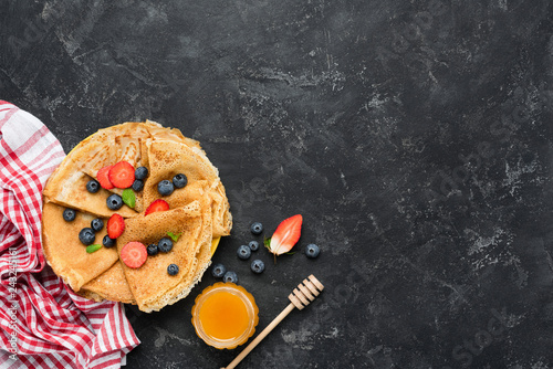 Tasty homemade crepes with honey and berries on black concrete background. Table top view. Maslenitsa food photo