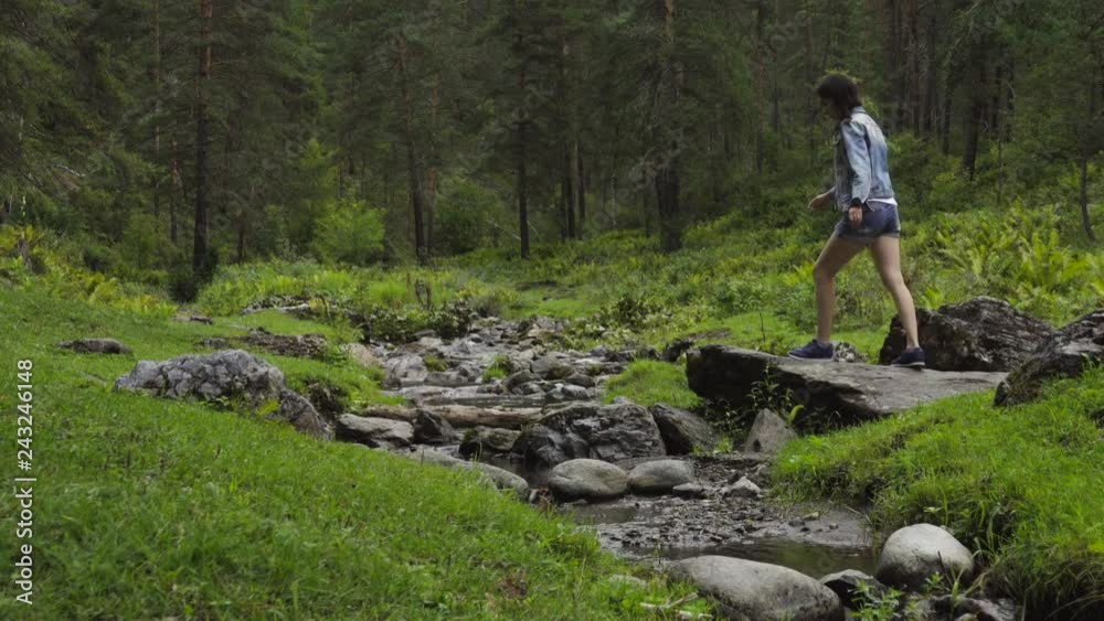 Girl walks on mountain stones on a river in the summer Girl walks on mountain stones on a river in the summer