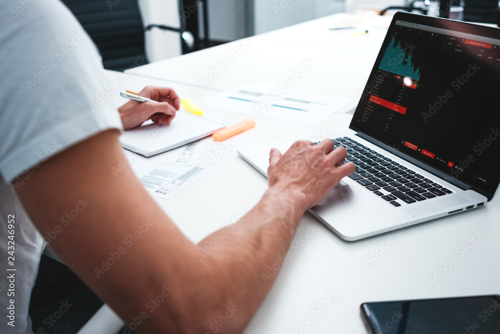 Businessman analyzing trends on screen laptop in space office. Back view of male manager sitting at desktop and monitoring statistics on monitor