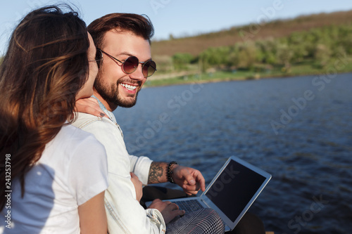 Cheerful couple using laptop near water