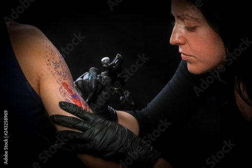 Female tattoo artist making tattoo on a men’s arm