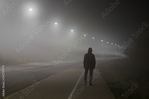 Fototapeta Young man alone slowly walking under white street lights in night