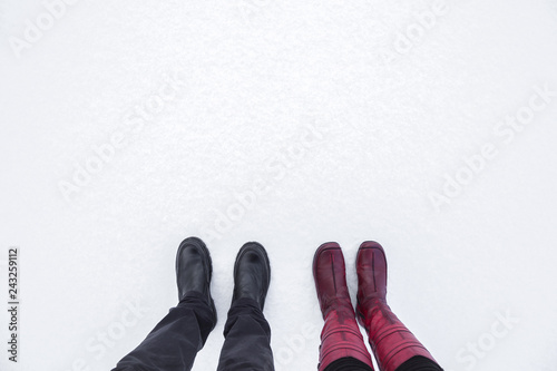 Young couple's boots standing beside each other on fresh, white snow. Enjoying stroll after snowstorm. Footwear for daily walking in winter season. Empty place for text, quote or sayings. Top view.