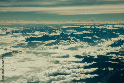 aerial view of himalayan black silhouettes desert mountains with snowy peaks under white clouds and blue sky