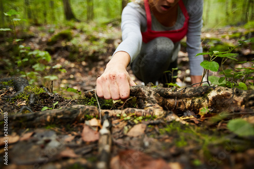 Hand of young sportswoman holding by dirty snag on the ground while moving forwards in the forest during training