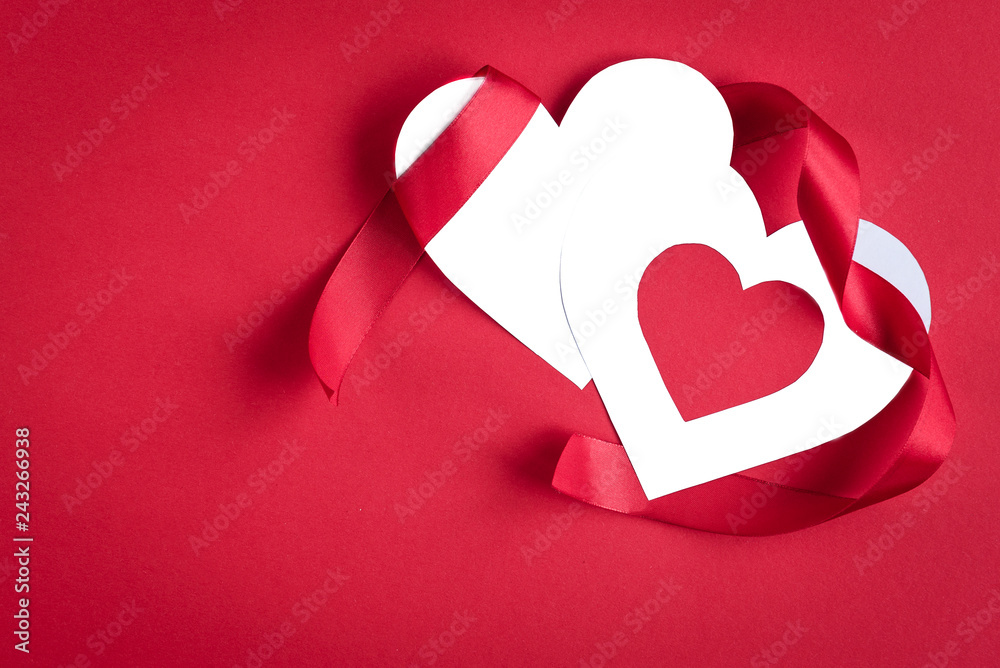 Two white paper valentine card heart with red ribbons and bow on red background with copy space.