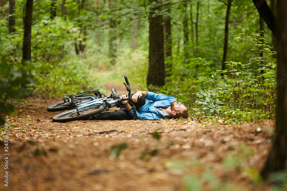 Active young man holding by his hurt or broken leg while lying on