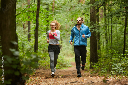 Fototapeta Naklejka Na Ścianę i Meble -  Young sporty couple running down forest path or in park in the morning between green trees