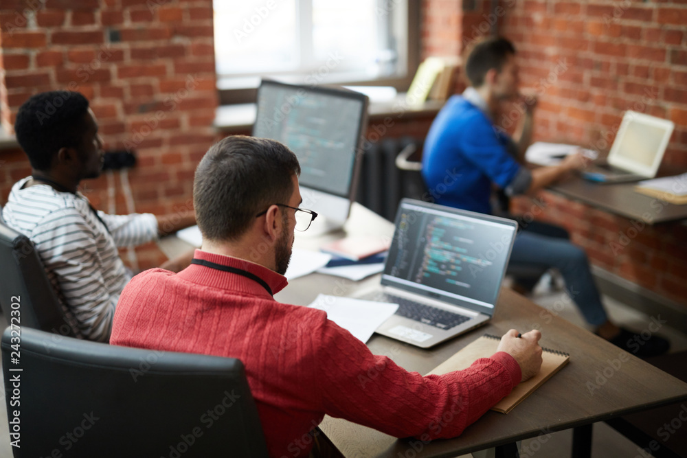 Group of contemporary it-engineers sitting b ydesks in front of computers and learning new software or codes Group of contemporary it-engineers sitting b ydesks in front of computers and learning new software or codes