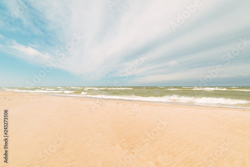 Fototapeta Naklejka Na Ścianę i Meble -  Sandy beach and blue sea with waves and seafoam. Background image for travel, summer vacation, and recreation. Vivid photo of tropical paradise.
