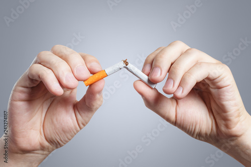 Close-up of male hands breaking a cigarette in half on grey background