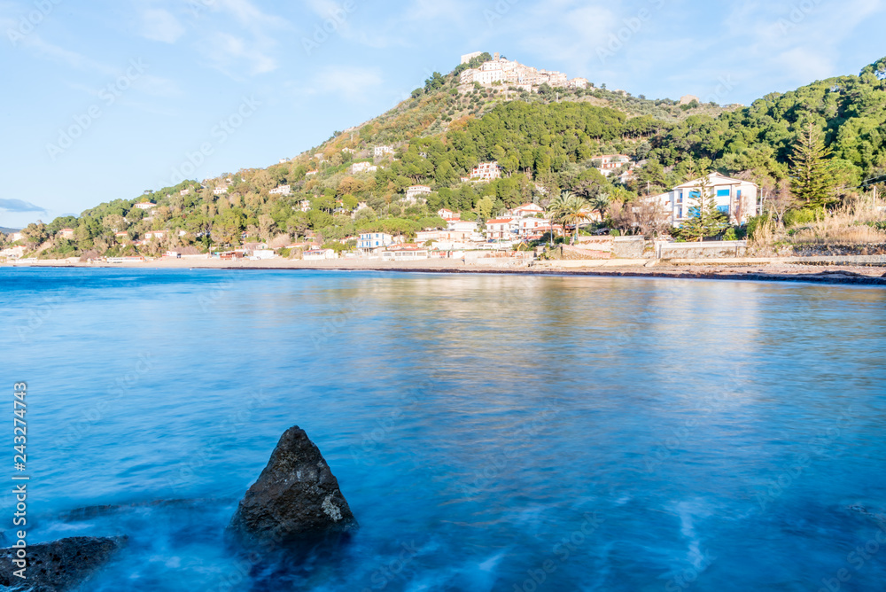 Fototapeta premium Long Exposure of the Mediterranean Sea Coast and a Medieval Hilltop Village with Blue Sky in Southern Italy