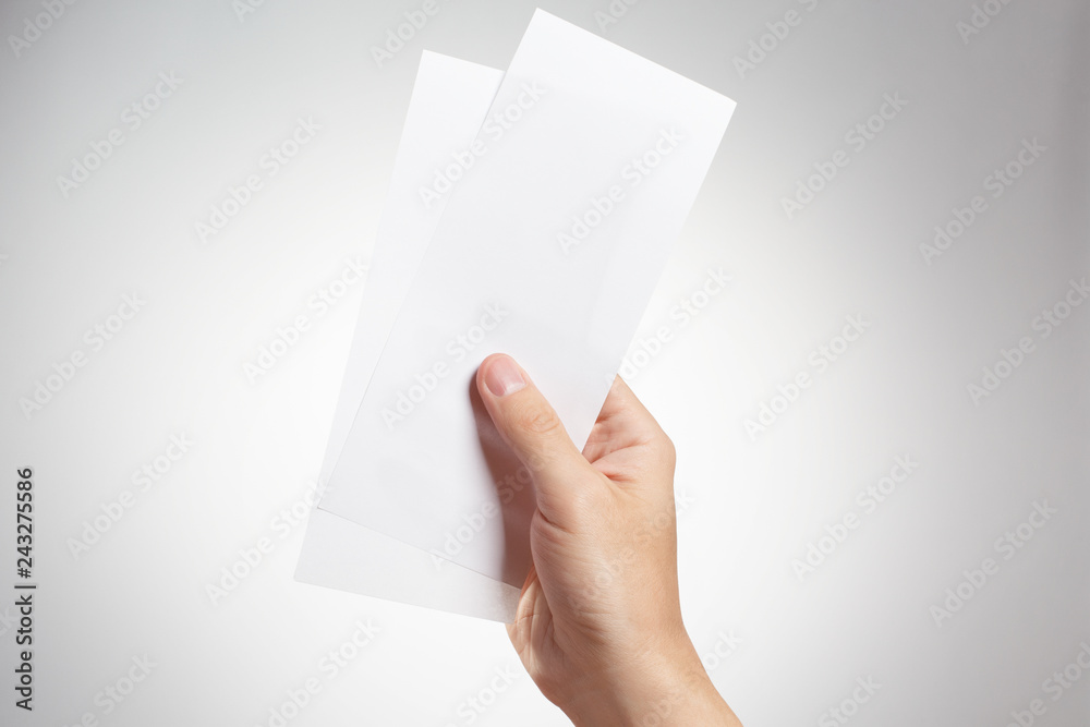 Male hand holding two blank sheets of paper (tickets, flyers, invitations, coupons, money, etc.), isolated on grey background Male hand holding two blank sheets of paper (tickets, flyers, invitations, coupons, money, etc.), isolated on grey background