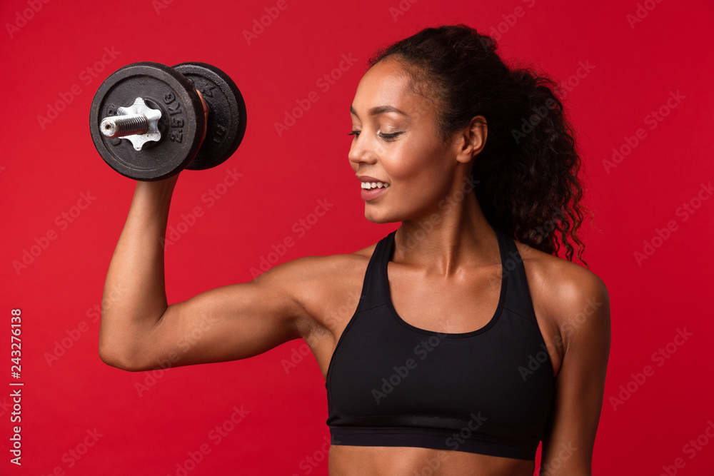 Image of beautiful african american woman in black sportswear lifting dumbbell, isolated over red background Image of beautiful african american woman in black sportswear lifting dumbbell, isolated over red background