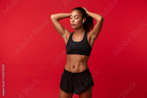 Beautiful young african sports fitness woman posing isolated over red wall background.