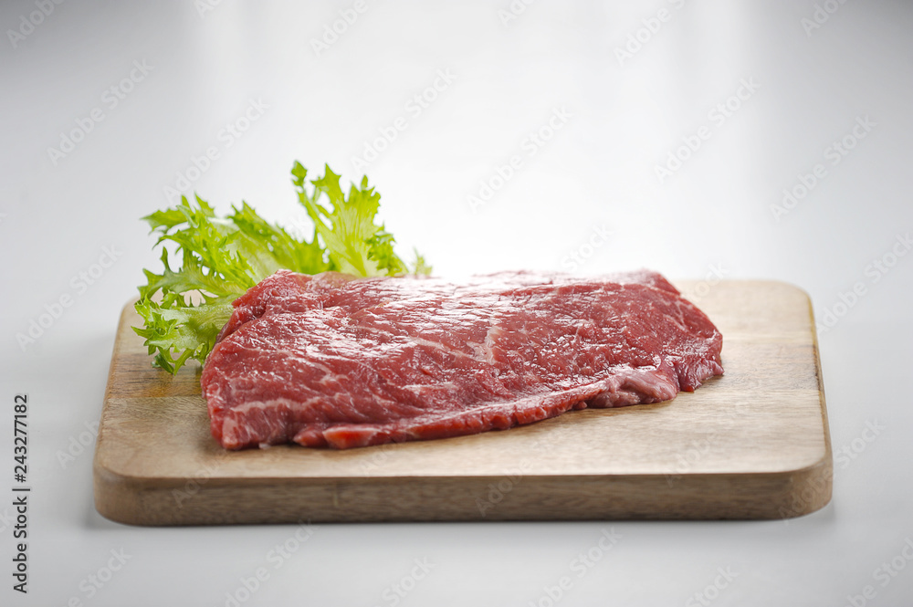 Beef steak on a wooden board. The steak is decorated with a leaf of green salad. Close-up. White background.