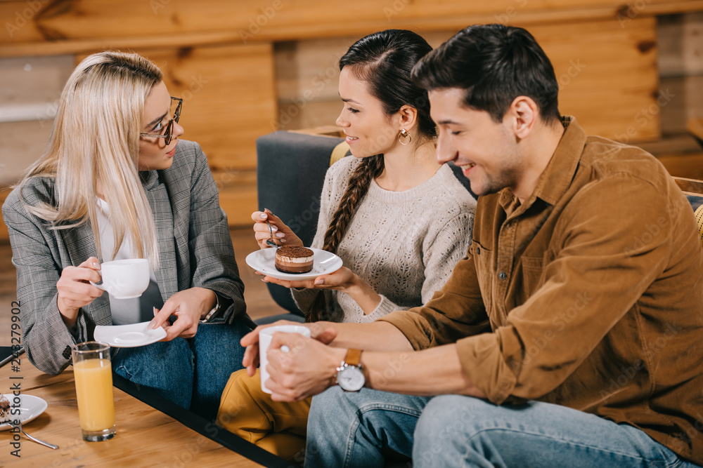 smiling woman chatting with friends while holding cake in cafe smiling woman chatting with friends while holding cake in cafe