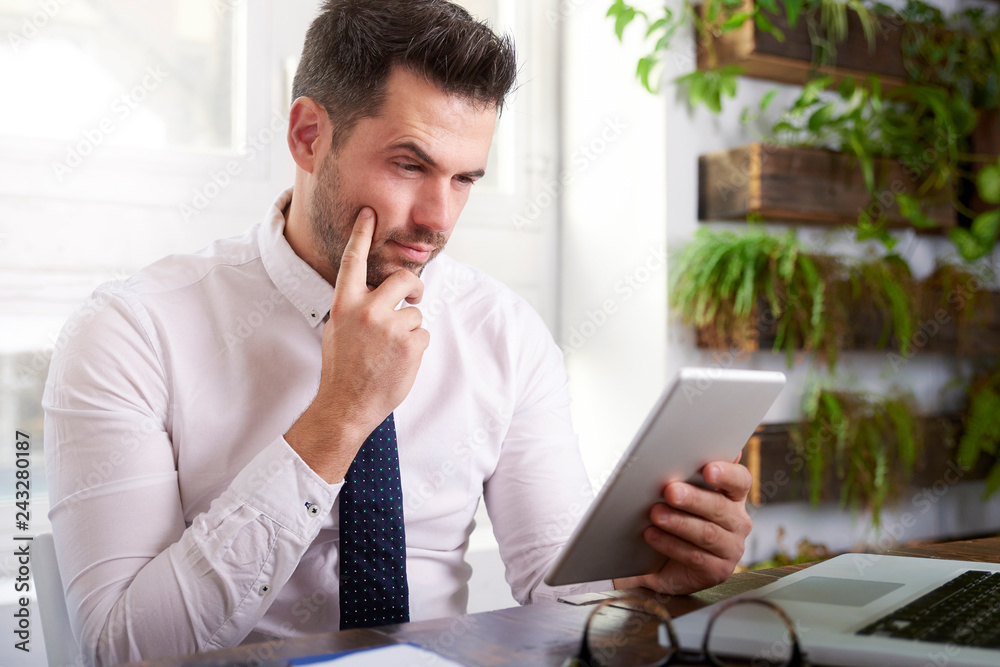 Naklejka premium Businessman using digital tablet and computer while sitting at desk and working in the office
