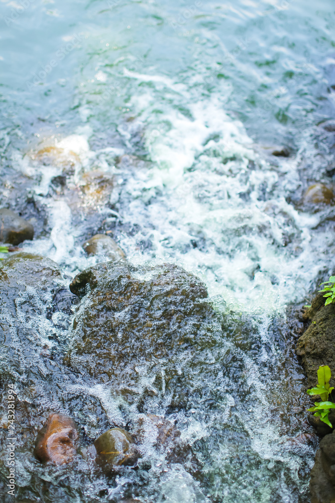 Top view of the creek. Water flows on stones. Bubbles and foam on the water. Abstract natural background.