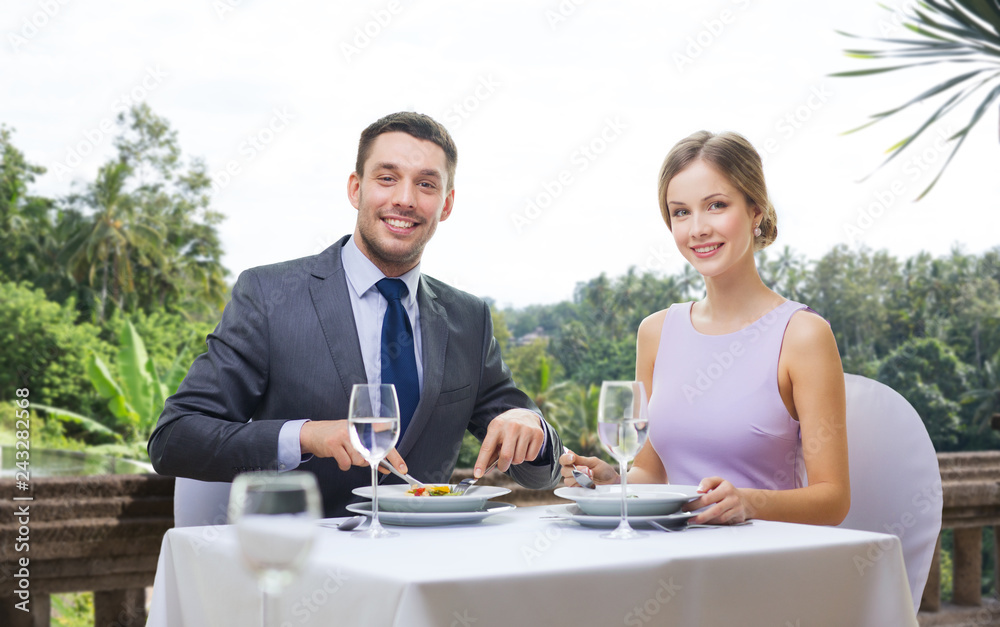 people and leisure concept - smiling couple eating appetizers at restaurant over summer background people and leisure concept - smiling couple eating appetizers at restaurant over summer background