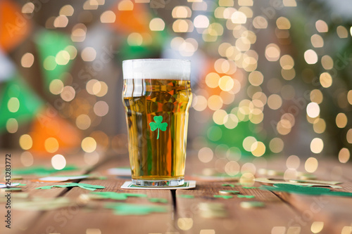st patricks day, holidays and celebration concept - glass of light beer with shamrock decoration and gold coins on wooden table