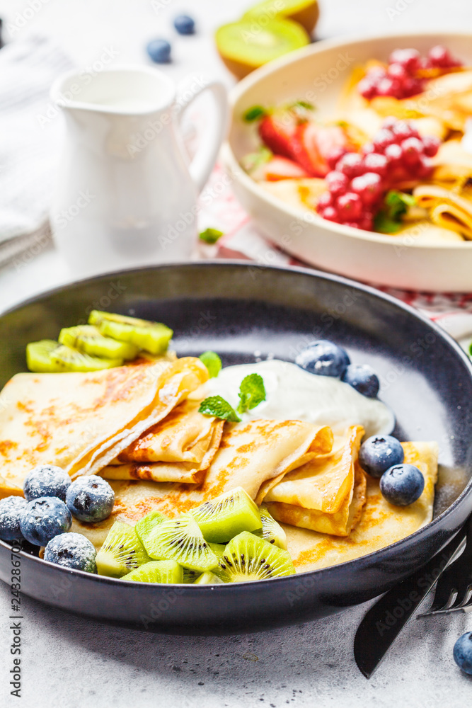 Homemade thin crepes served with curd cream, fruits and berries in black and white plates. Homemade thin crepes served with curd cream, fruits and berries in black and white plates.