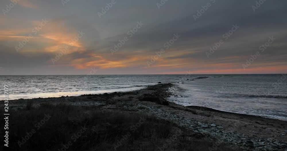Time lapse of twilight over the sea on a stone covered beach with tall grass Time lapse of twilight over the sea on a stone covered beach with tall grass