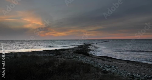 Time lapse of twilight over the sea on a stone covered beach with tall grass