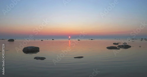 Sunset time lapse over a calm sea with large boulders