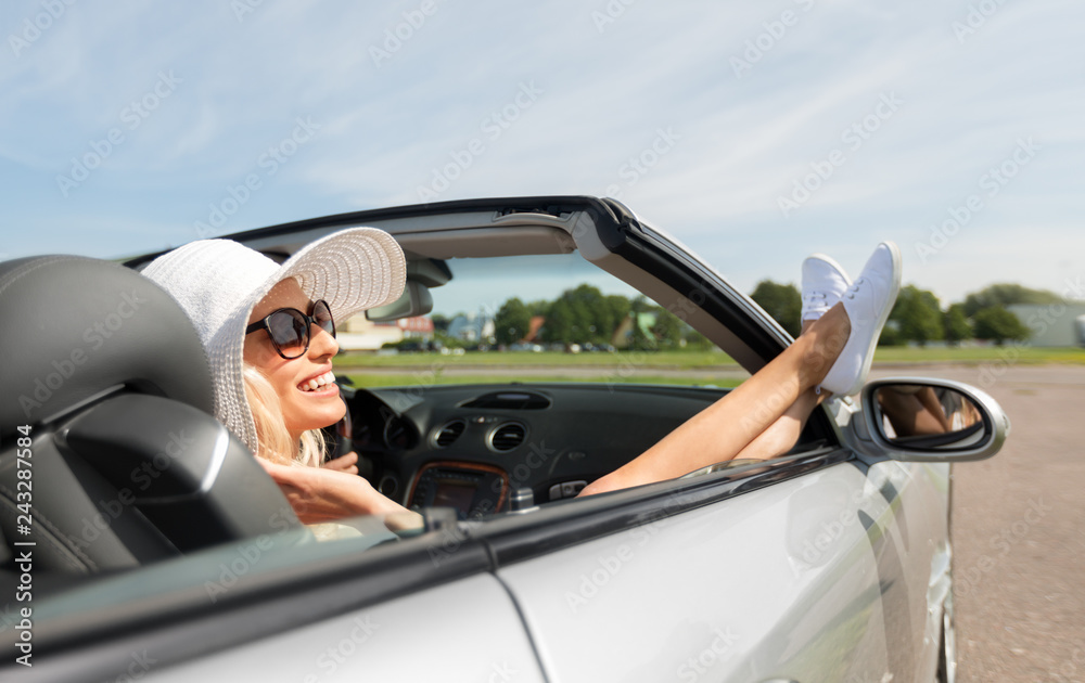 Naklejka premium transport, leisure and people concept - happy woman in summer hat and sunglasses chilling in cabriolet car outdoors