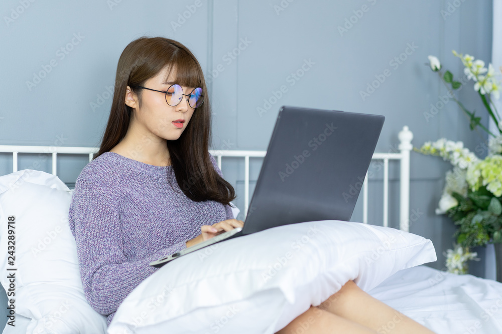 Asian woman working on bed .She dress sweater violet colour.Morning check email internet from notebook. Asian woman working on bed .She dress sweater violet colour.Morning check email internet from notebook.