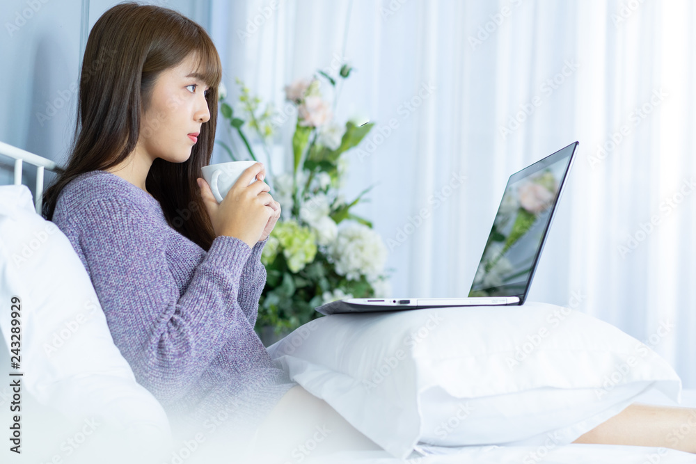 Asian woman working on bed .She dress sweater violet colour.Morning check email internet from notebook. Asian woman working on bed .She dress sweater violet colour.Morning check email internet from notebook.