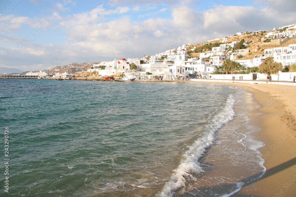 Beautiful sand beach in the foreground, with a typical church in the distance, Mykonos town, Cyclades, Greece.