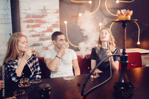 Hookah smoking shisha in bar and nightclub, team of friends laugh, talk and drink Arabic tea