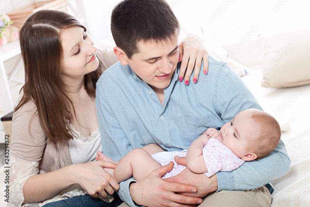 Family concept - baby with dad and mom. Portrait of happy young parents with baby in the bed at home.