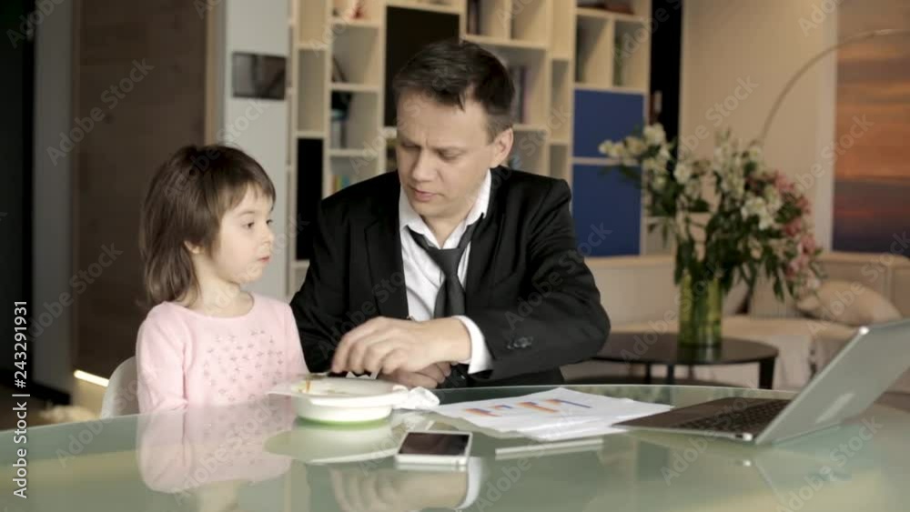 Father in suit working with papers and feeding daughter Father in suit working with papers and feeding daughter