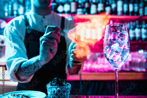 Expert barman is making cocktail at night club or bar. Glass of fiery cocktail on the bar counter against the background of bartenders hands with fire. Barman day concept