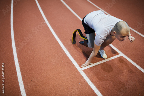 Young runner with handicapped right leg bending over start line on stadium ready to run marathon photo