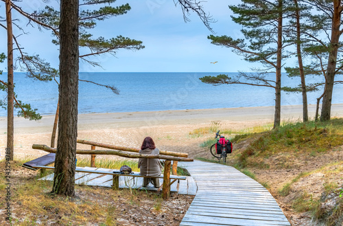 Happy woman is resting on wooden bench and  looking at the distance on sandy ...