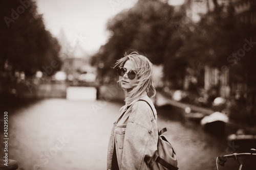 Canvas Print Young girl in red sweater and orange sunglasses with backpack at bridge in Amsterdam street