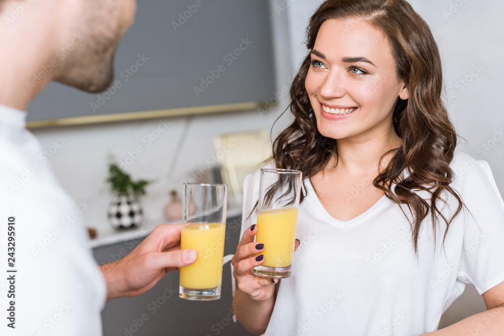 selective focus of attractive woman smiling while holding glass with orange juice near boyfriend selective focus of attractive woman smiling while holding glass with orange juice near boyfriend